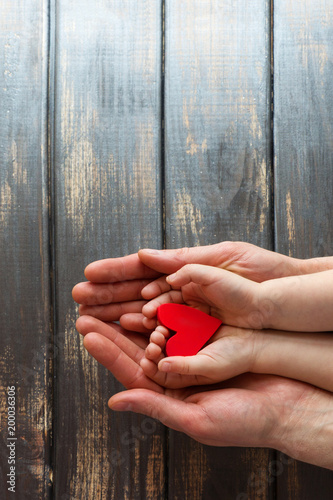 Two pairs of hands, men and children on a wooden background. Four hands are holding a red, bright heart.