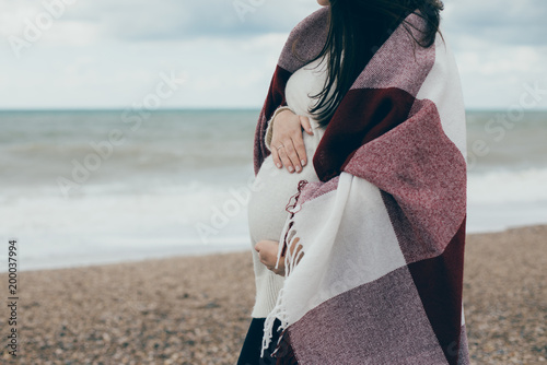 Young beautiful pragnant woman in a white knitted sweater posing near sea at the beach photo