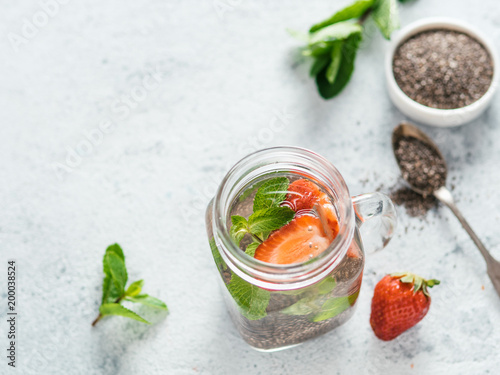 View from above chia water in mason jar with strawberry and mint on gray cement background. Chia infused detox water with berries. Copy space for text. Healthy eating, drinks, diet, detox concept