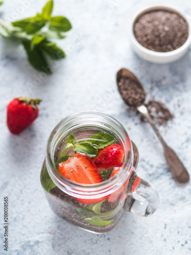 View from above chia water in mason jar with strawberry and mint on gray cement background. Chia infused detox water with berries. Healthy eating, drinks, diet, detox concept. Vertocal