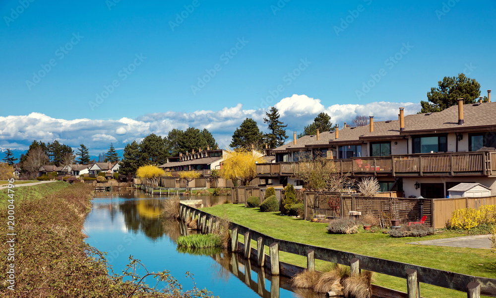 
A village of townhouses at the picturesque outskirts of the city of Richmond. Along the row of townhouses flows a creek  against the background of a blue sky and a mountain ridge