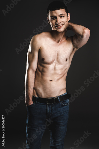 Portrait of satisfied male stripped to waist while keeping head by arm. He isolated on black background