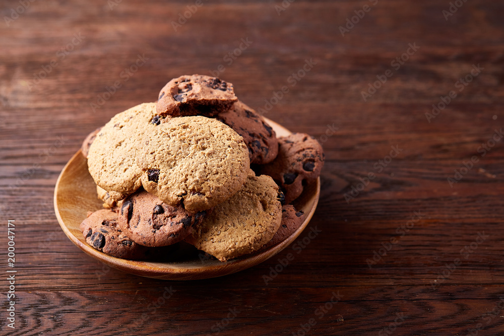 Fototapeta premium Side view of chocolate chip cookies on a wooden plate over rustic background, selective focus