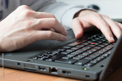 White man hands typing on a black notebook keyboard with natural light.