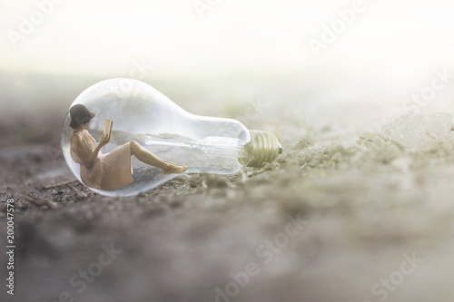 surreal image of a small woman reading inside a light bulb photo