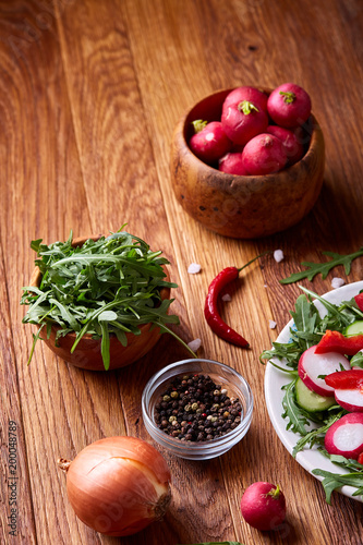 Fresh red radish in wooden bowl among plates with vegetables, herbs and spicies, top view, selective focus.