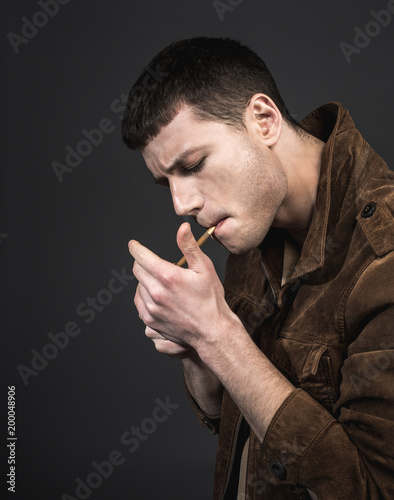 Side view serious male setting fire to cigarette. He isolated on black background. Demure guy concept