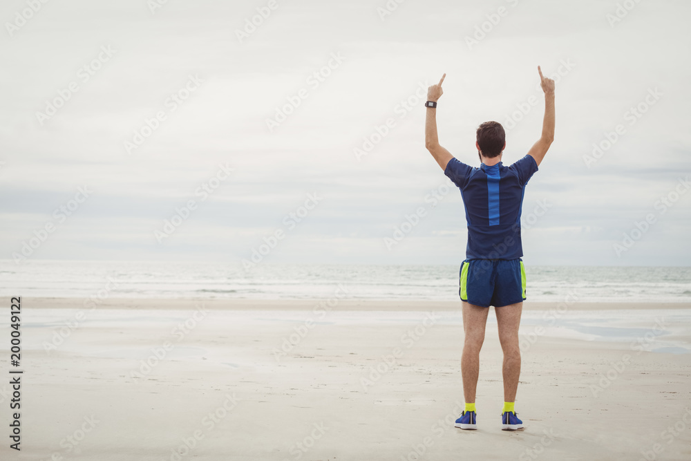 Happy athlete standing on the beach with his hands raised Happy athlete standing on the beach with his hands raised
