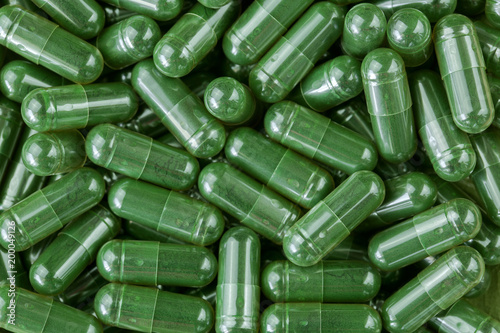 Green Spirulina powder, blue-green algae in clear capsules photo