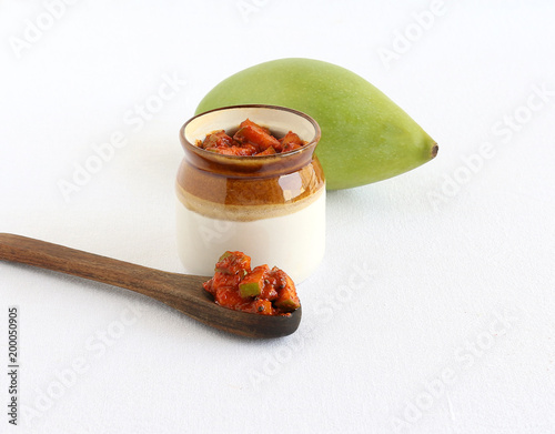 Pickles, an Indian vegetarian, traditional and popular side dish made from a type of mango known as totapuri, on a wooden spoon and in a jar, and in the background is the fruit. photo