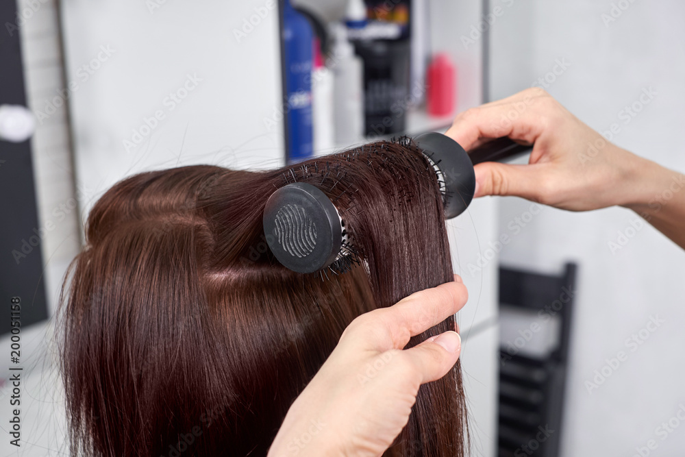 Naklejka premium Closeup of hair dresser combing client's hair in salon