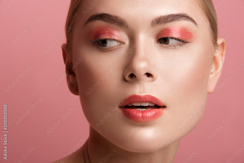 Close up of female expression with daily maquillage looking aside. Her skin having healthy tone. Isolated on rose background