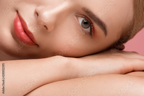 Close up of female half face looking with wistfulness. Her skin is cared and healthy. Isolated on rose background