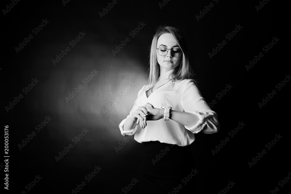 Studio portrait of blonde businesswoman in glasses, white blouse and black skirt against dark background. Successful woman. Girl looking at watches.