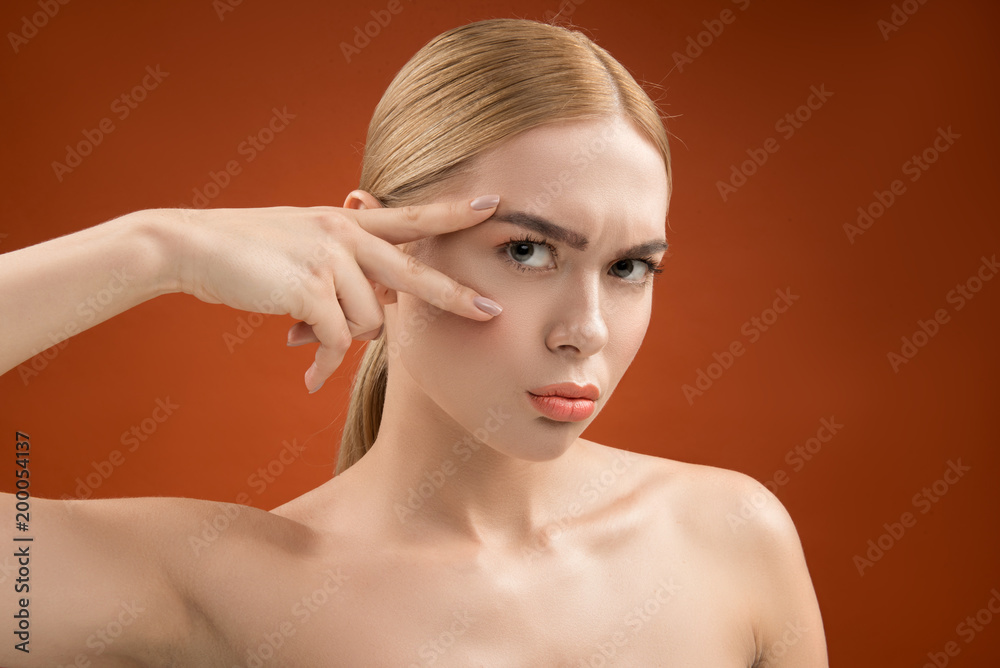 Naklejka premium Portrait of severe woman with naked shoulders and fresh skin. She is looking at camera through victory gesture. Isolated on background