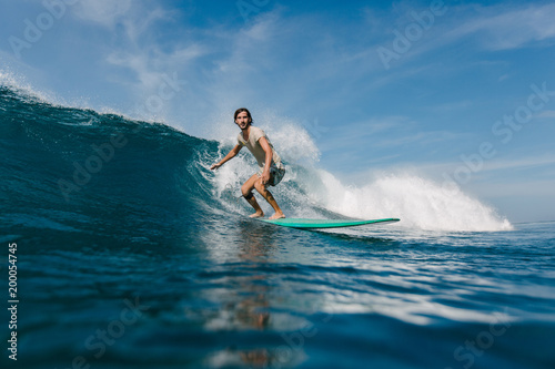 bearded young man in wet t-shirt riding waves on surfboard on sunny day
