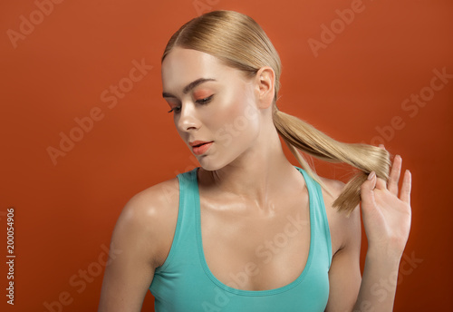 Haircare concept. Calm female person watching down. She is touching her well cared straight hair in ponytail. Isolated on background