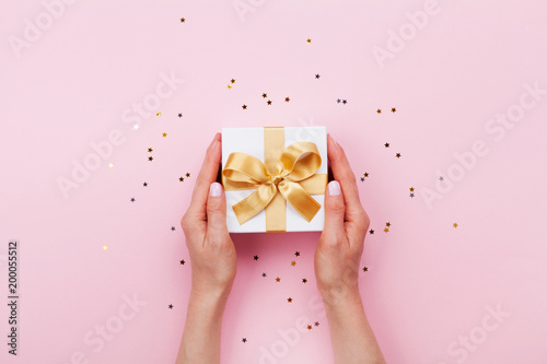 Womans hands holding gift or present box decorated confetti on pink pastel table top view. Flat lay composition for birthday or wedding. photo