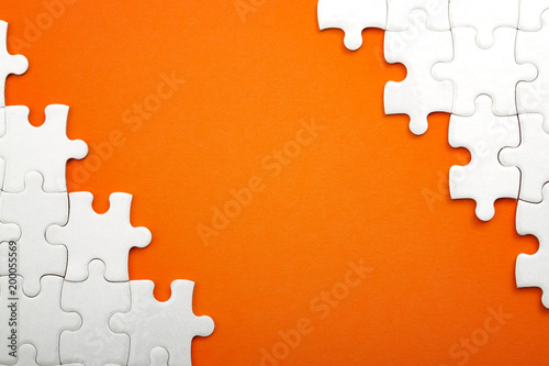 Jigsaw puzzle pieces and business concept with a border made of puzzle pieces on colorful bright orange background with copy space