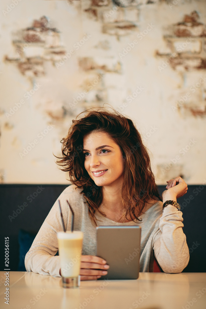 Young caucasian woman using tablet while sitting in cafe and drinking coffee. Young caucasian woman using tablet while sitting in cafe and drinking coffee.
