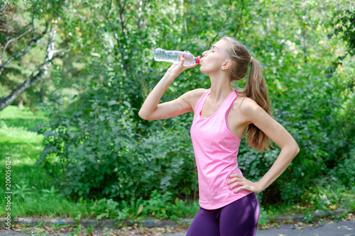 Sporty young woman drinking water from the bottle. Doing Sport Outdoor.