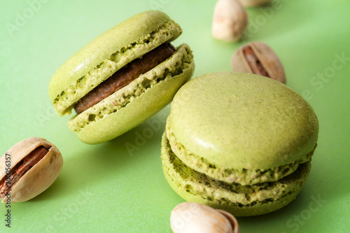 French dessert, sweet meringue based confectionery and expensive sweets concept with close up on green pistachio flavored macaroon or macaron with a bunch of pistachios on green background