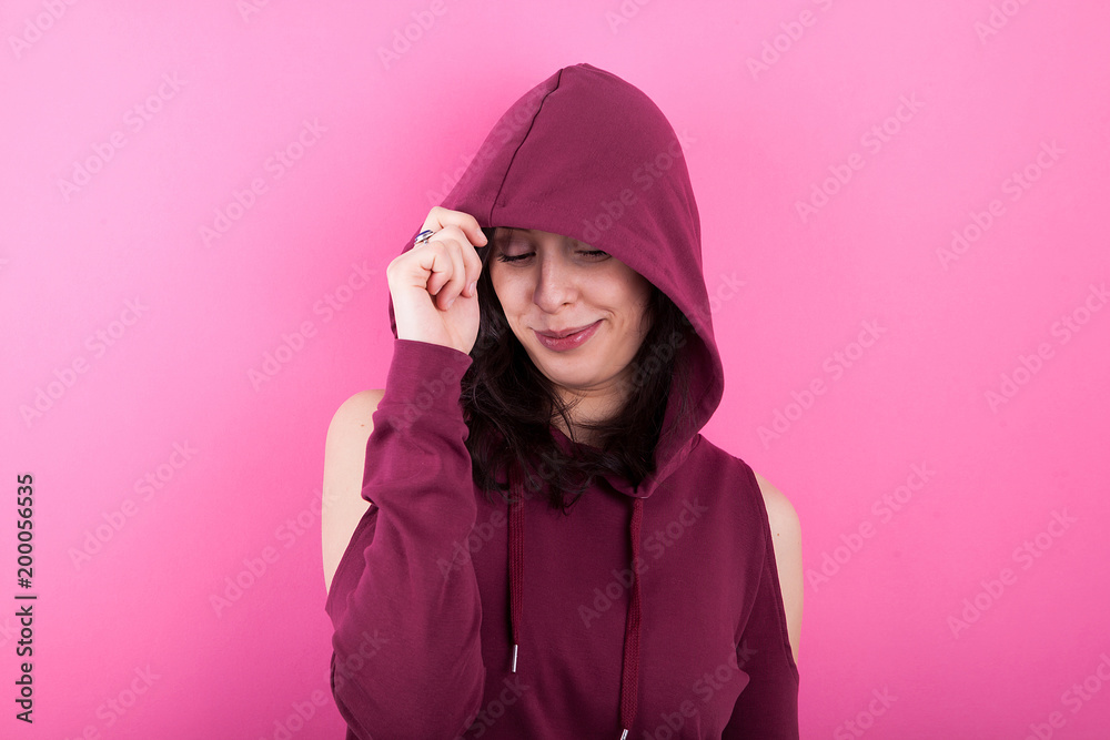 Portrait of beautiful young woman wearing a hood on pink background in studio Portrait of beautiful young woman wearing a hood on pink background in studio