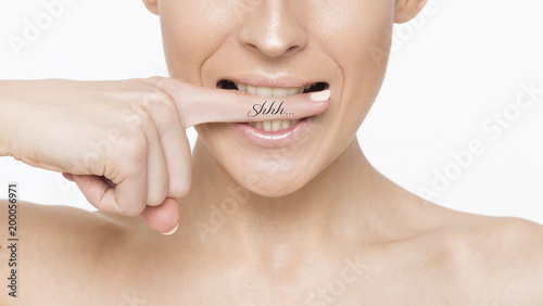 Close up Photo of a beautiful smiling female face with clean and fresh skin, the girl puts a finger to her lips.