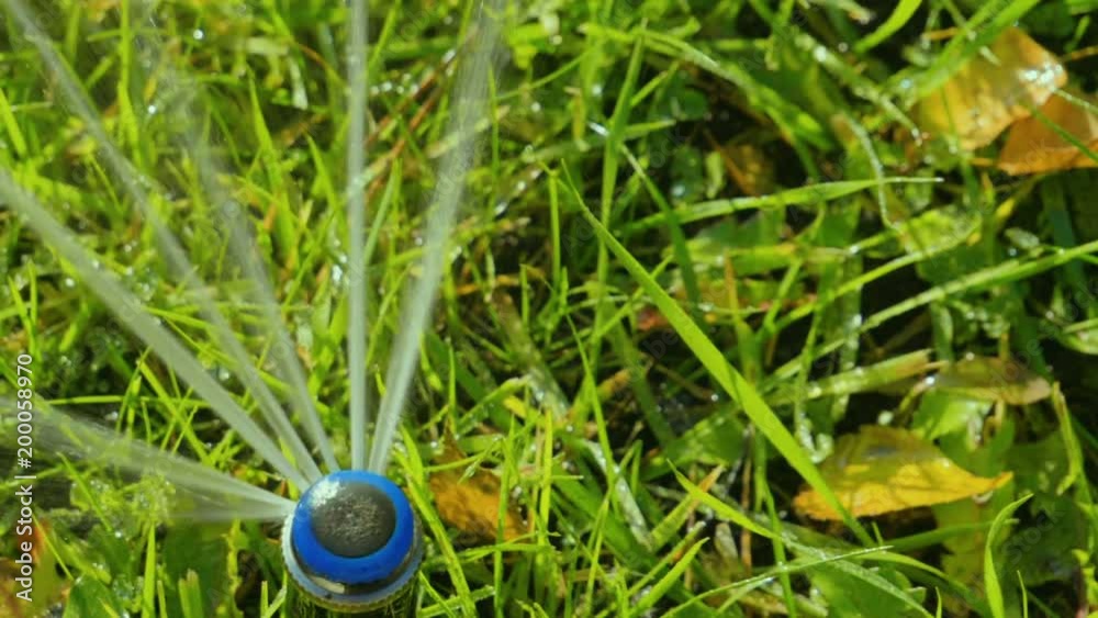 Close-up of a nozzle for spraying water by automatic watering system for lawn with lush green grass in sunny day. Slow motion. HD Close-up of a nozzle for spraying water by automatic watering system for lawn with lush green grass in sunny day. Slow motion. HD