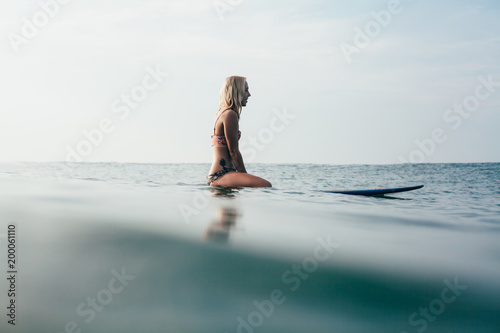 Photography side view of young attractive woman sitting on surfboard in water