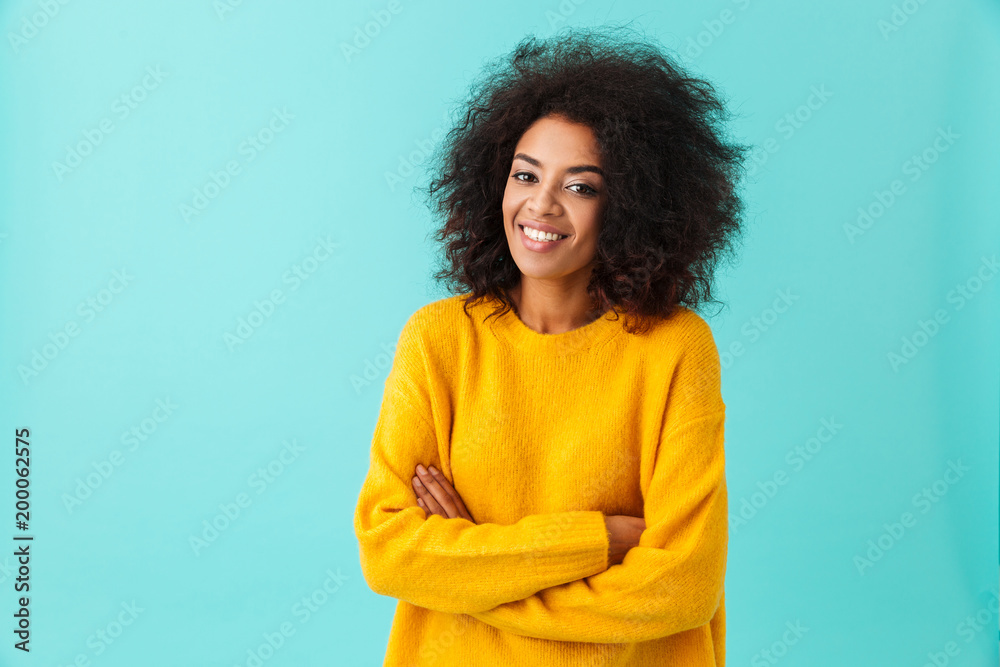 Happy brunette woman in yellow shirt looking on camera with perfect smile standing with arms crossed, isolated over blue background - obrazy, fototapety, plakaty 