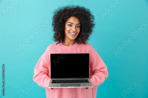 Portrait of cheerful woman 20s holding laptop and demonstrating copyspace black screen, isolated over blue background