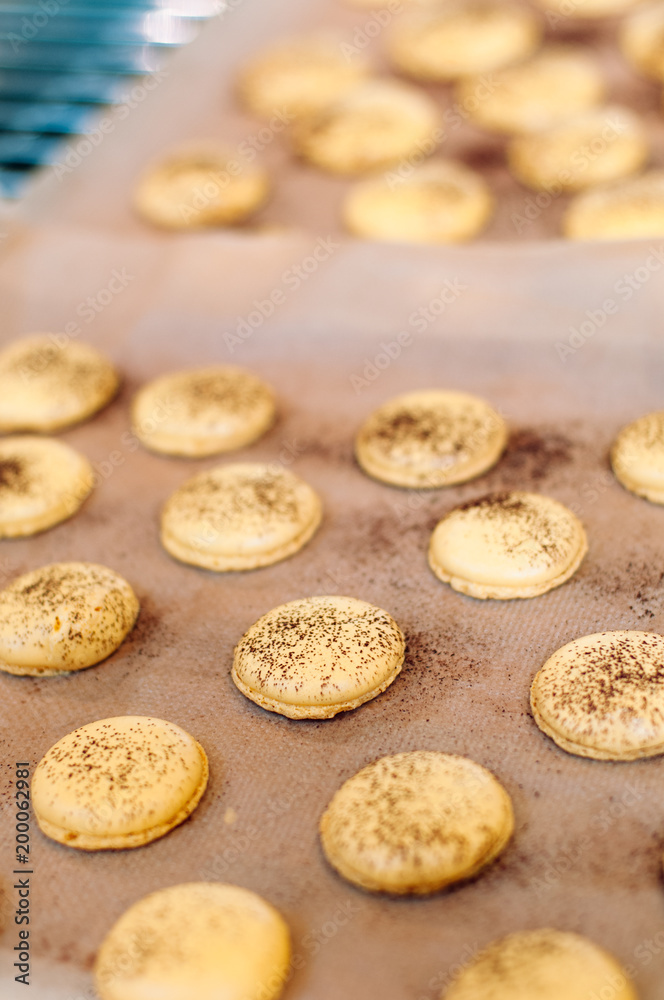 Freshly baked, yellow French Macaron with passion fruit flavor dusted with cocoa powder on silicone mat at baking workshop in France