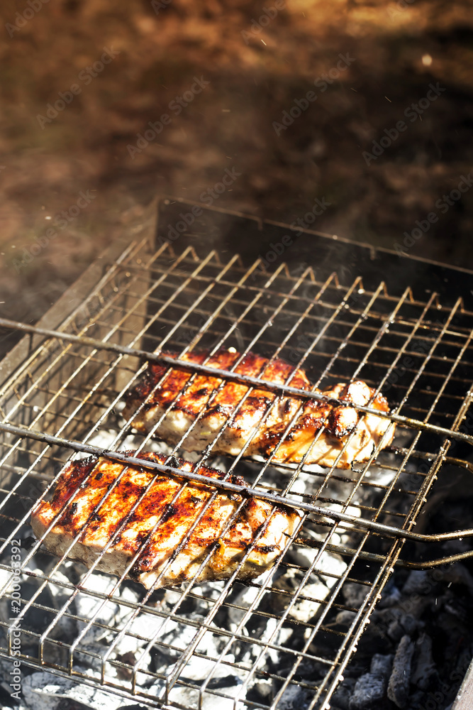 Two pork steaks on the grid are prepared on the grill outdoor. Summer family barbecue concept