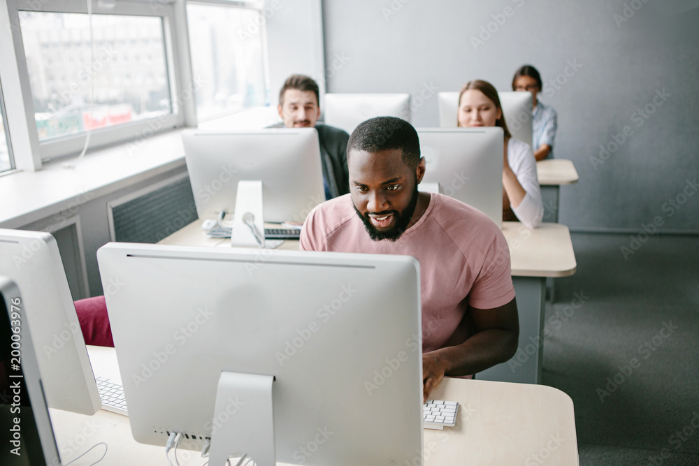 Obraz premium Young people sitting at table and using computer in light office.