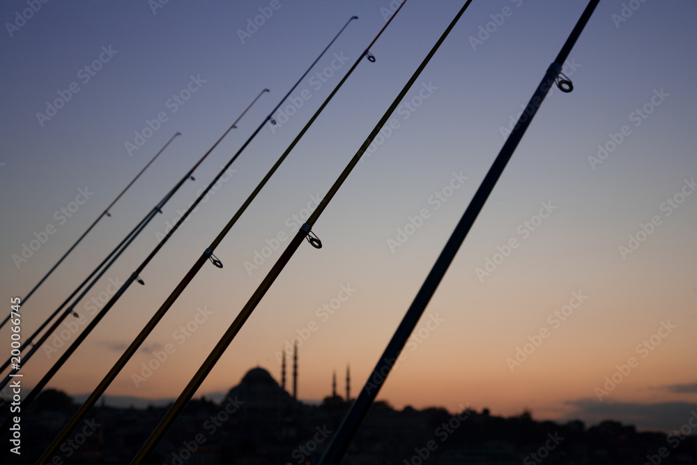 A row of fishing rods and distant mosque silhouetted at sunset from Galata bridge in Istanbul, Turkey. A row of fishing rods and distant mosque silhouetted at sunset from Galata bridge in Istanbul, Turkey.