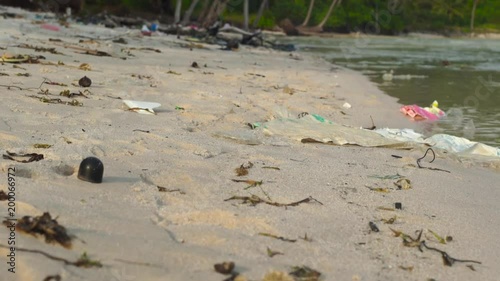 Slowmotion steadycam shot of a beach with fine white sand covered with garbage photo