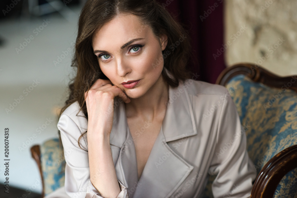 portrait of elegant lady in beige trench coat sitting in armchair portrait of elegant lady in beige trench coat sitting in armchair