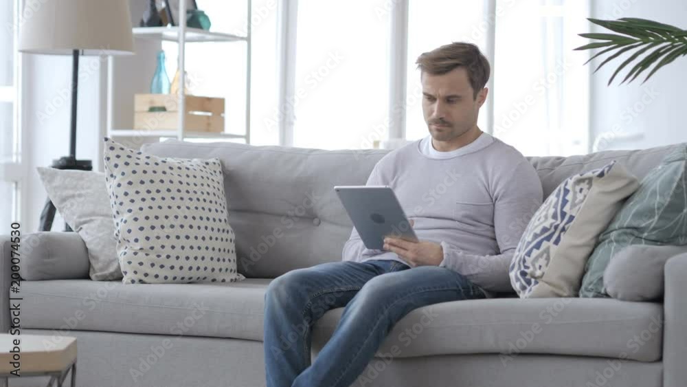 Adult Man Sitting on Couch and using Tablet Adult Man Sitting on Couch and using Tablet