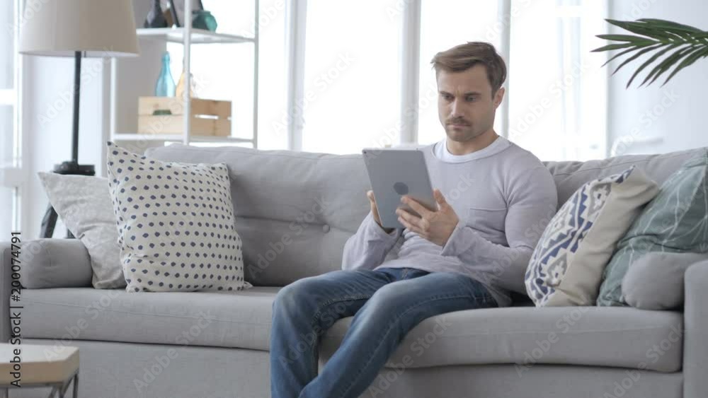 Serious Man using Tablet while Sitting on Sofa Serious Man using Tablet while Sitting on Sofa