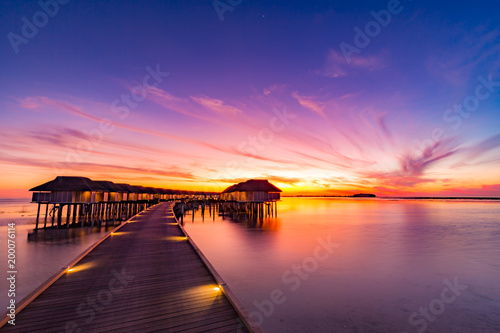 Sunset in Maldives island. Beautiful sunset sky and clouds, luxury water villas and wooden pathway - pier