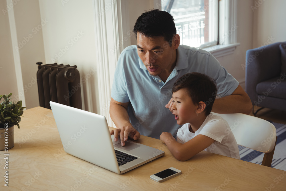 Father and son using mobile phone and laptop in living room Father and son using mobile phone and laptop in living room