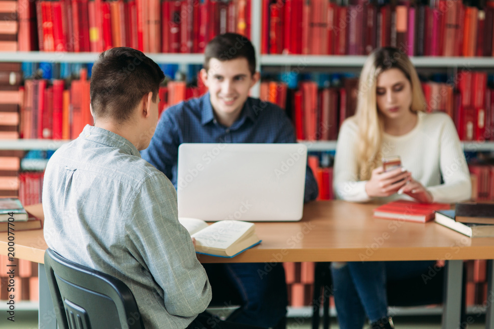 University students sitting together at table with books and laptop. Happy young people doing group study in library University students sitting together at table with books and laptop. Happy young people doing group study in library