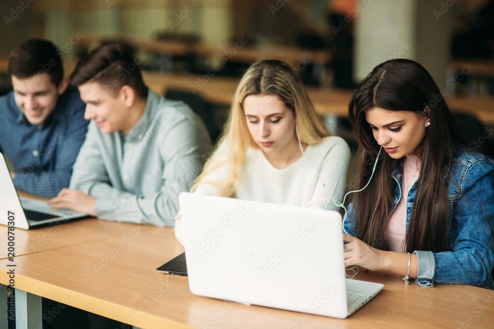 Group of college students studying in the school library, a girl and a boy are using a laptop and connecting to internet Group of college students studying in the school library, a girl and a boy are using a laptop and connecting to internet