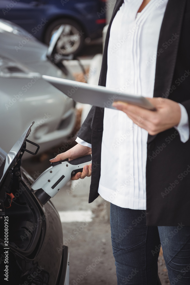 Mid section of woman using digital tablet while charging electric car Mid section of woman using digital tablet while charging electric car