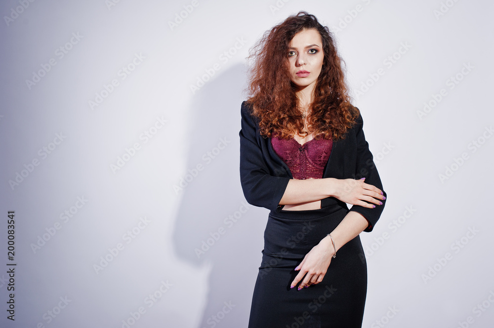 Brunette curly haired girl in black office jacket with skirt, on bra at studio against white background. Sexy businesswoman. Brunette curly haired girl in black office jacket with skirt, on bra at studio against white background. Sexy businesswoman.