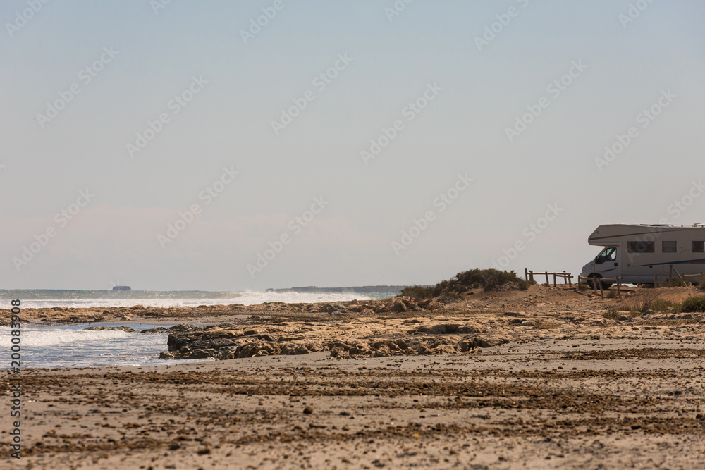 Caravan motorhome parked on the beach in front of the blue sea in a beautiful place of wild nature