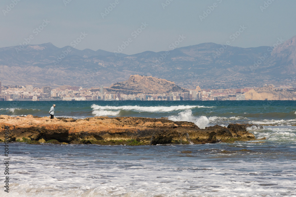 Fearless older woman facing the bustling sea and gale in Alicante, Spain