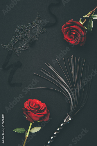 Black whip and lacy mask with rose flowers isolated on black photo