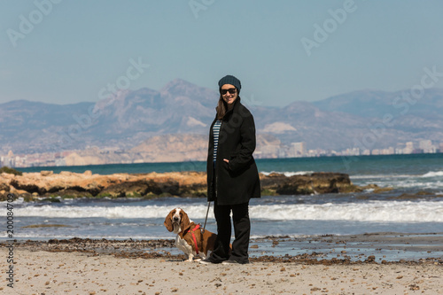 Girl and her basset hound dog walking along the beach in the winter sun